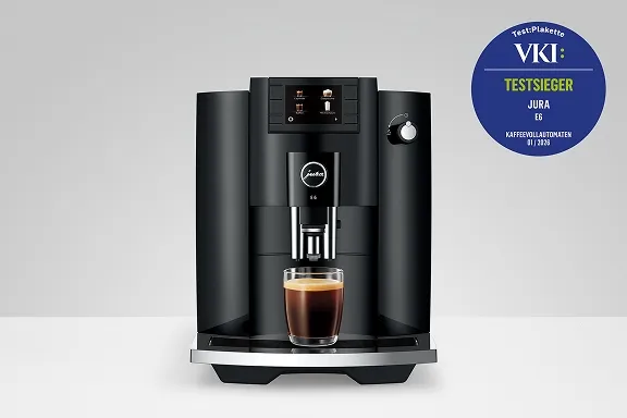 Frontalansicht des schwarzen Jura E6 Kaffeevollautomaten mit einem frisch gebrühten Kaffee und VKI-Siegel.