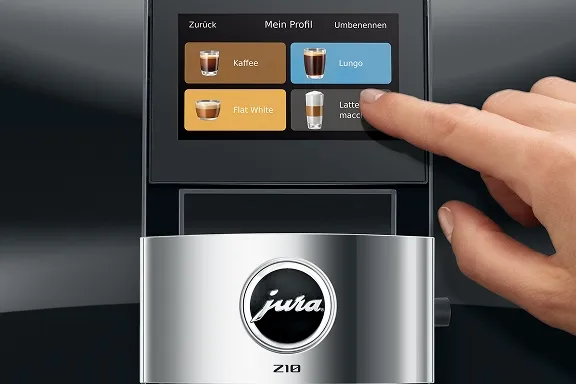 Nahaufnahme einer Hand, die auf dem Touch-Display einer silbernen Jura Z10 Kaffeemaschine ein Getränk wählt.